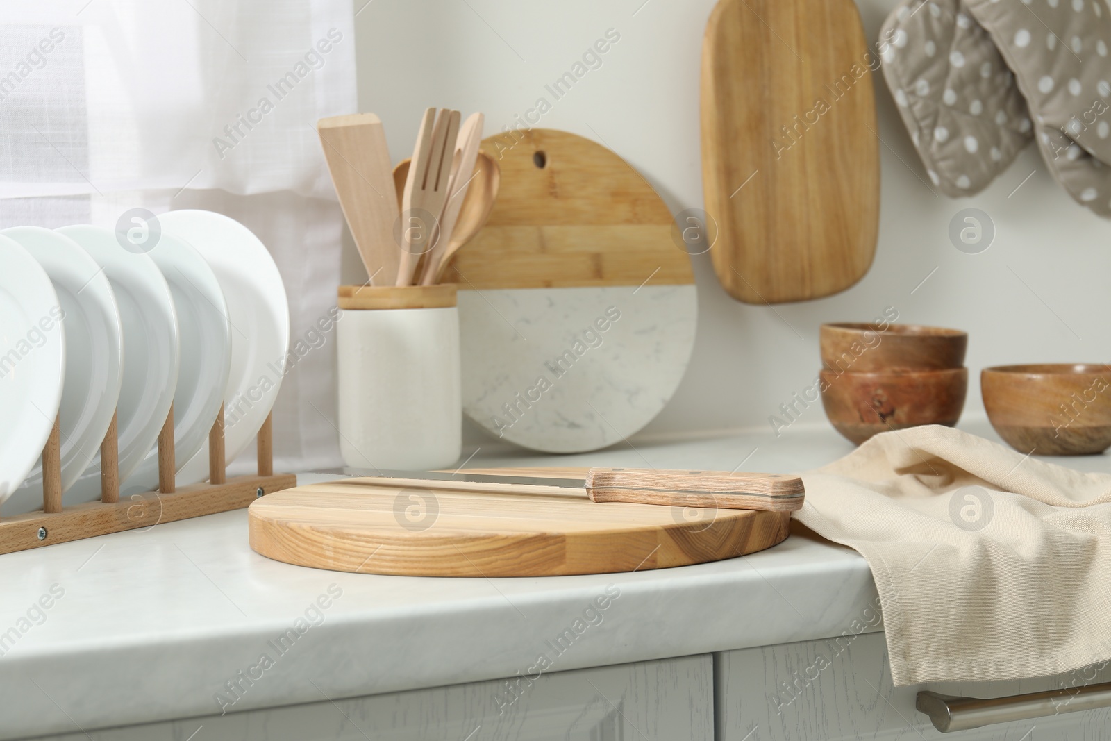 Photo of Wooden cutting boards, other cooking utensils and dishware on white countertop in kitchen