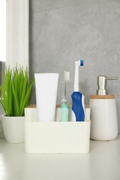 Photo of Electric toothbrushes and tube of paste on white countertop in bathroom