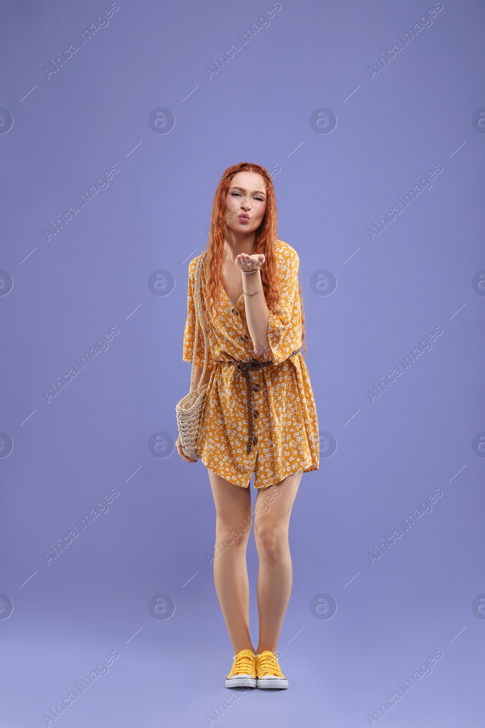 Photo of Stylish young hippie woman blowing kiss on violet background