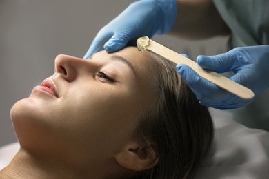 Photo of Young woman undergoing hair removal procedure on face with sugaring paste in salon