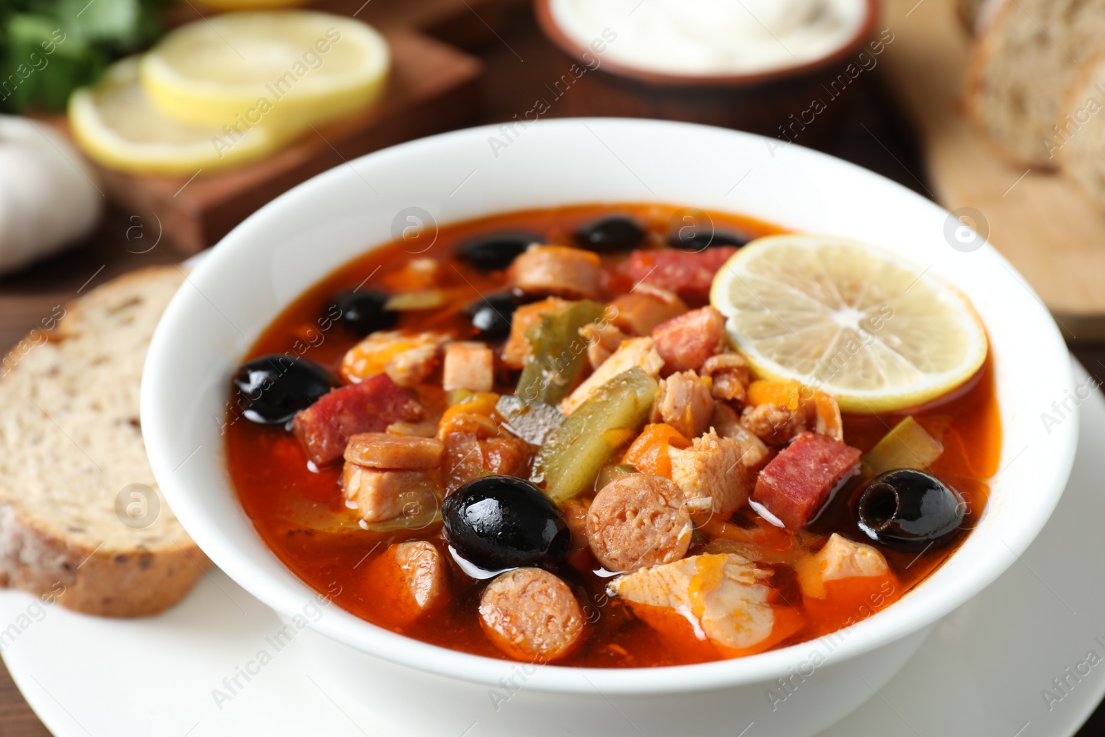 Photo of Meat solyanka soup with sausages, olives and vegetables on table, closeup