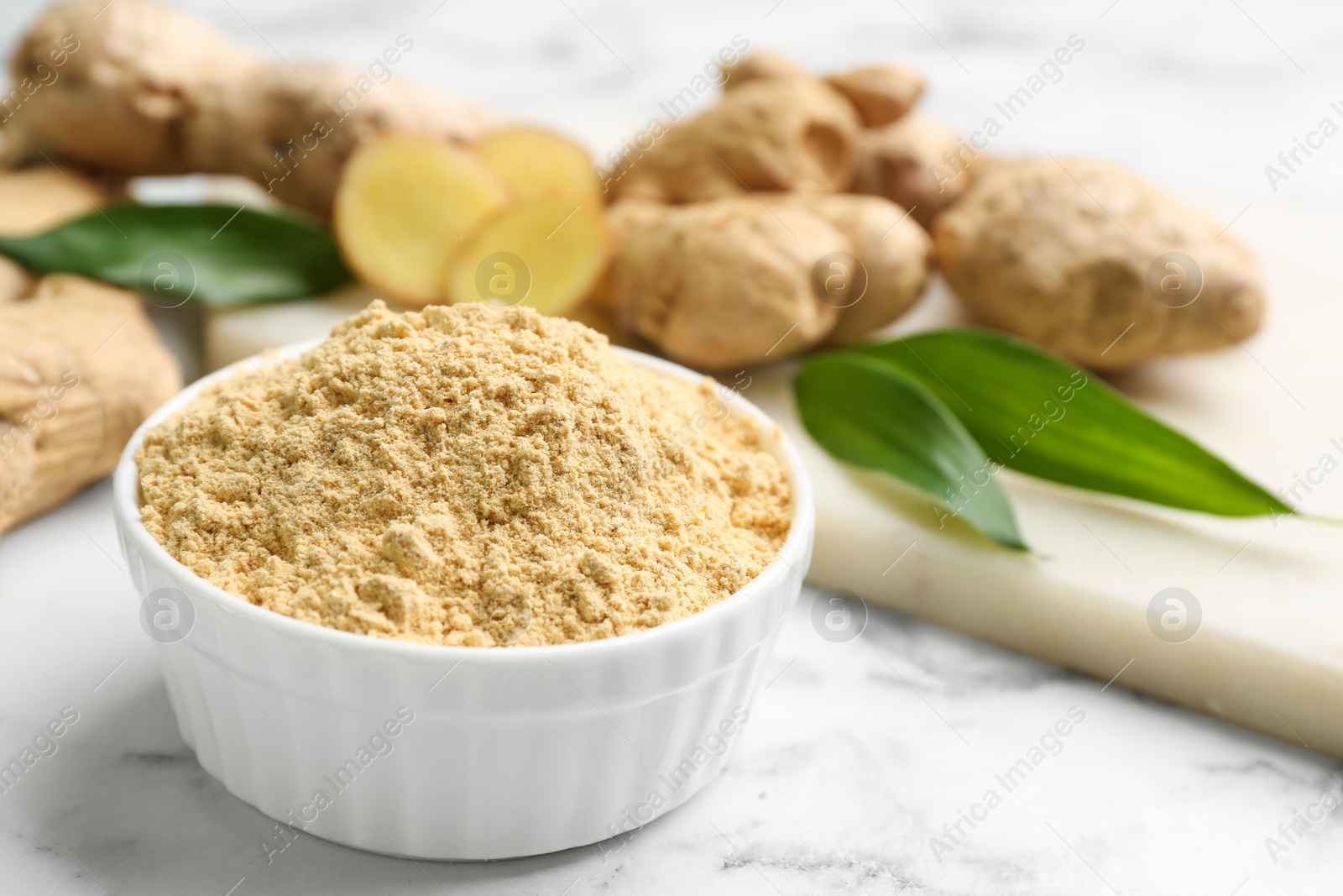 Photo of Dry ginger powder and fresh root on white marble table. Space for text