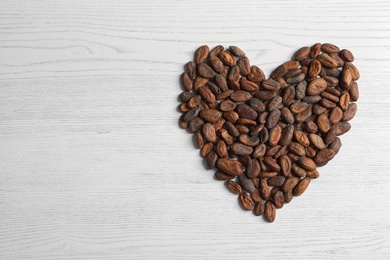 Heart made of cocoa beans on white wooden table, top view. Space for text