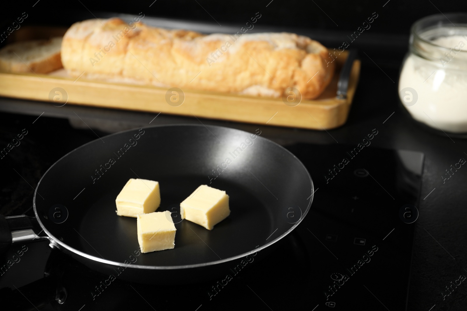 Photo of Melting butter in frying pan, bread and flour on black table