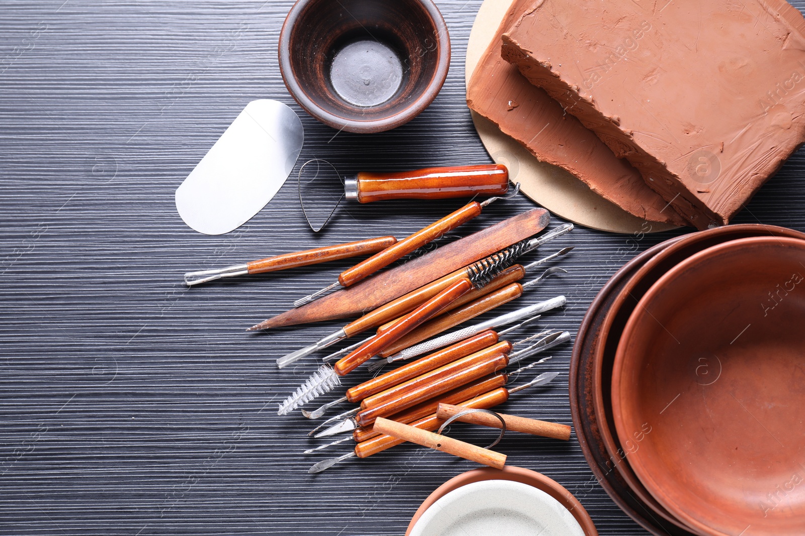 Photo of Clay, dishes and set of crafting tools on black table, flat lay