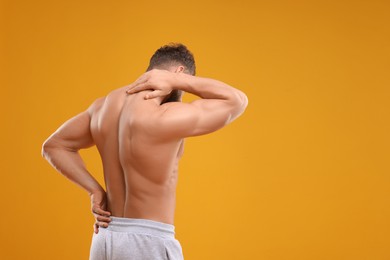 Photo of Man suffering from back and neck pain on orange background, space for text
