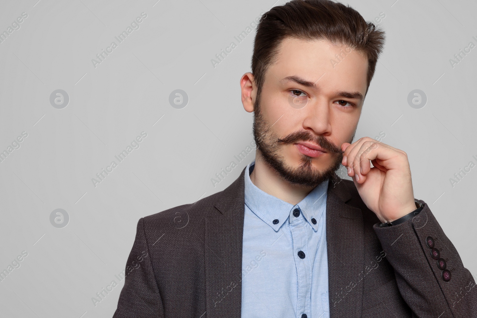 Photo of Handsome man in suit touching mustache on light grey background. Space for text