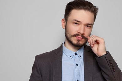 Photo of Handsome man in suit touching mustache on light grey background. Space for text