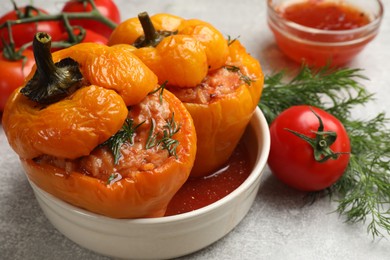 Photo of Tasty stuffed peppers in bowl, dill and tomato on light grey table, closeup