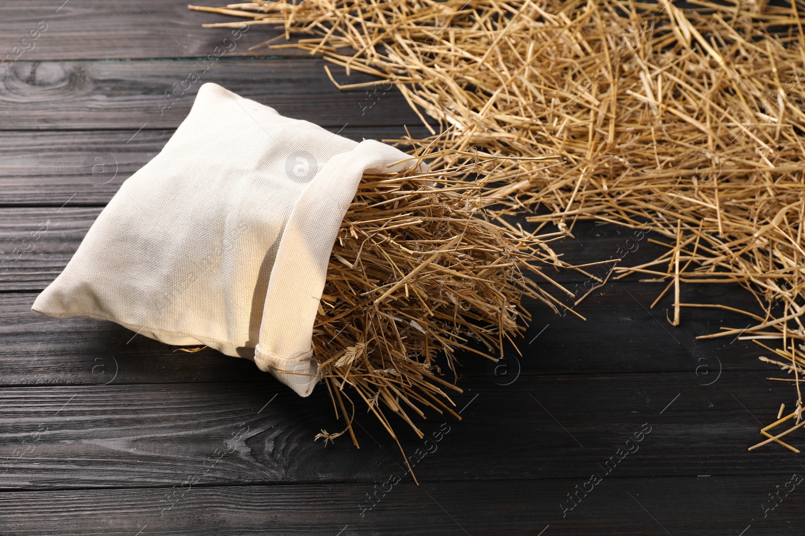 Photo of Dried straw in burlap sack on dark wooden table