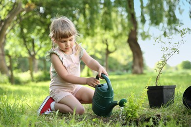 Cute little girl watering tree in garden