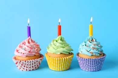 Photo of Birthday cupcakes with burning candles on light blue background
