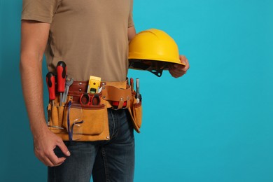 Photo of Professional builder with hard hat and tool belt on light blue background, closeup. Space for text