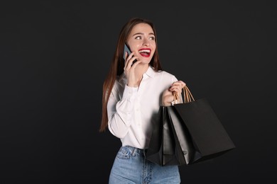 Photo of Happy young woman with shopping bags and smartphone on black background. Big sale