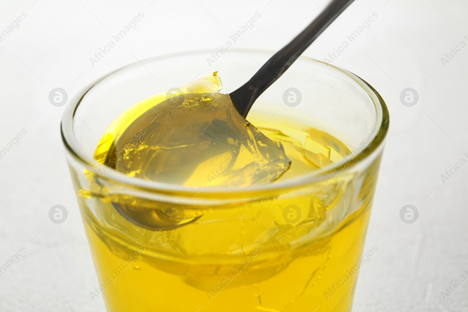 Photo of Spoon with fruit jelly over glass on light background, closeup