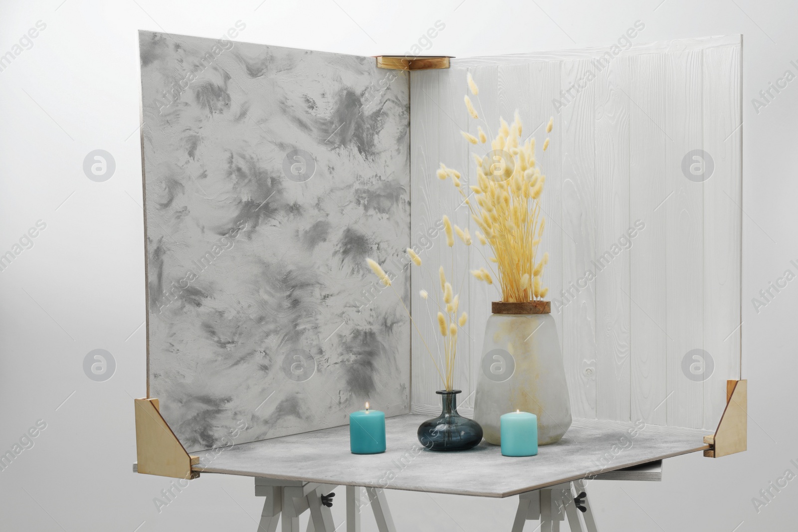 Photo of Vases with beautiful dry flowers, candles and double-sided backdrops on table in photo studio