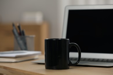 Photo of Black ceramic mug and laptop on wooden table at workplace