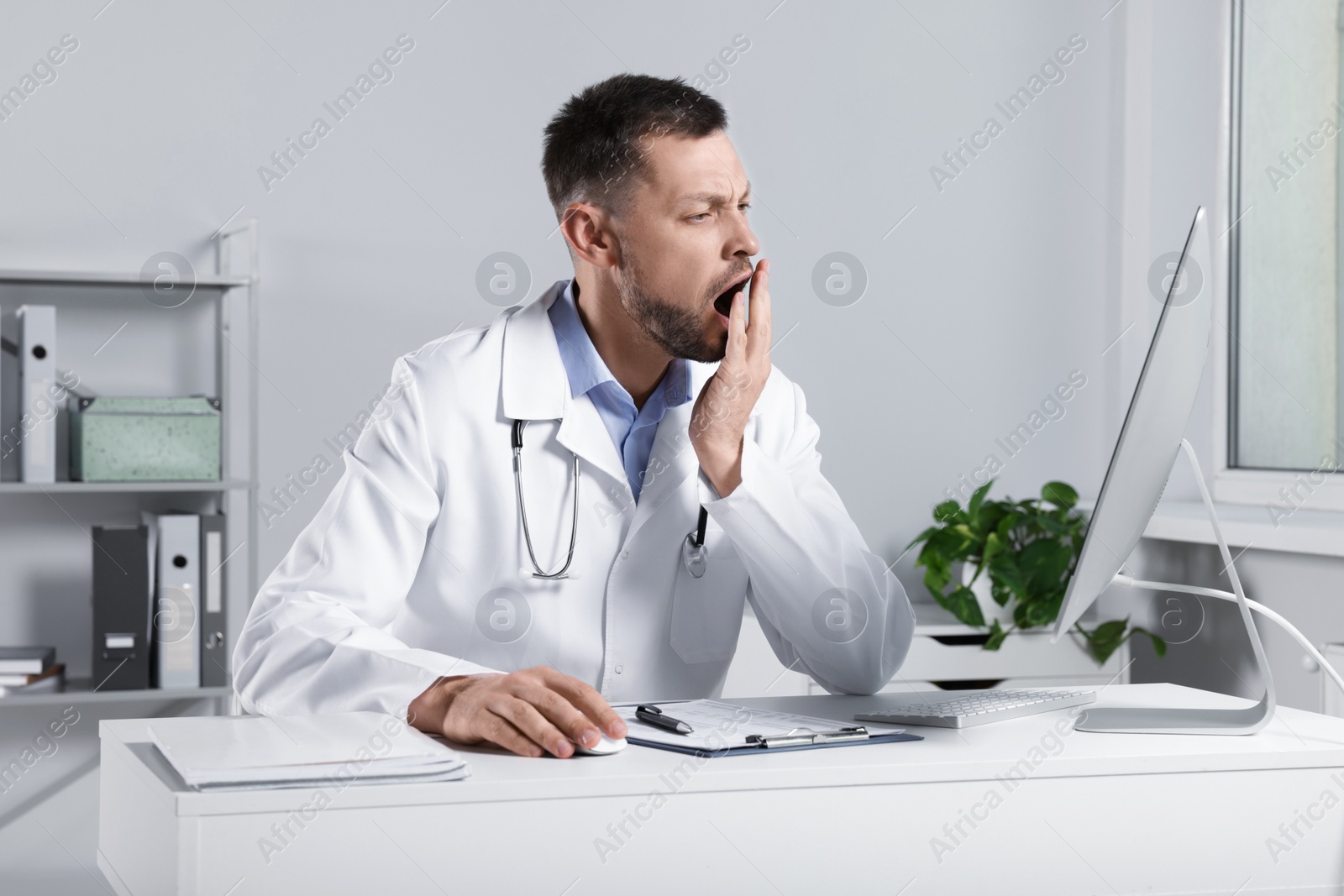 Photo of Exhausted doctor yawning at workplace in hospital