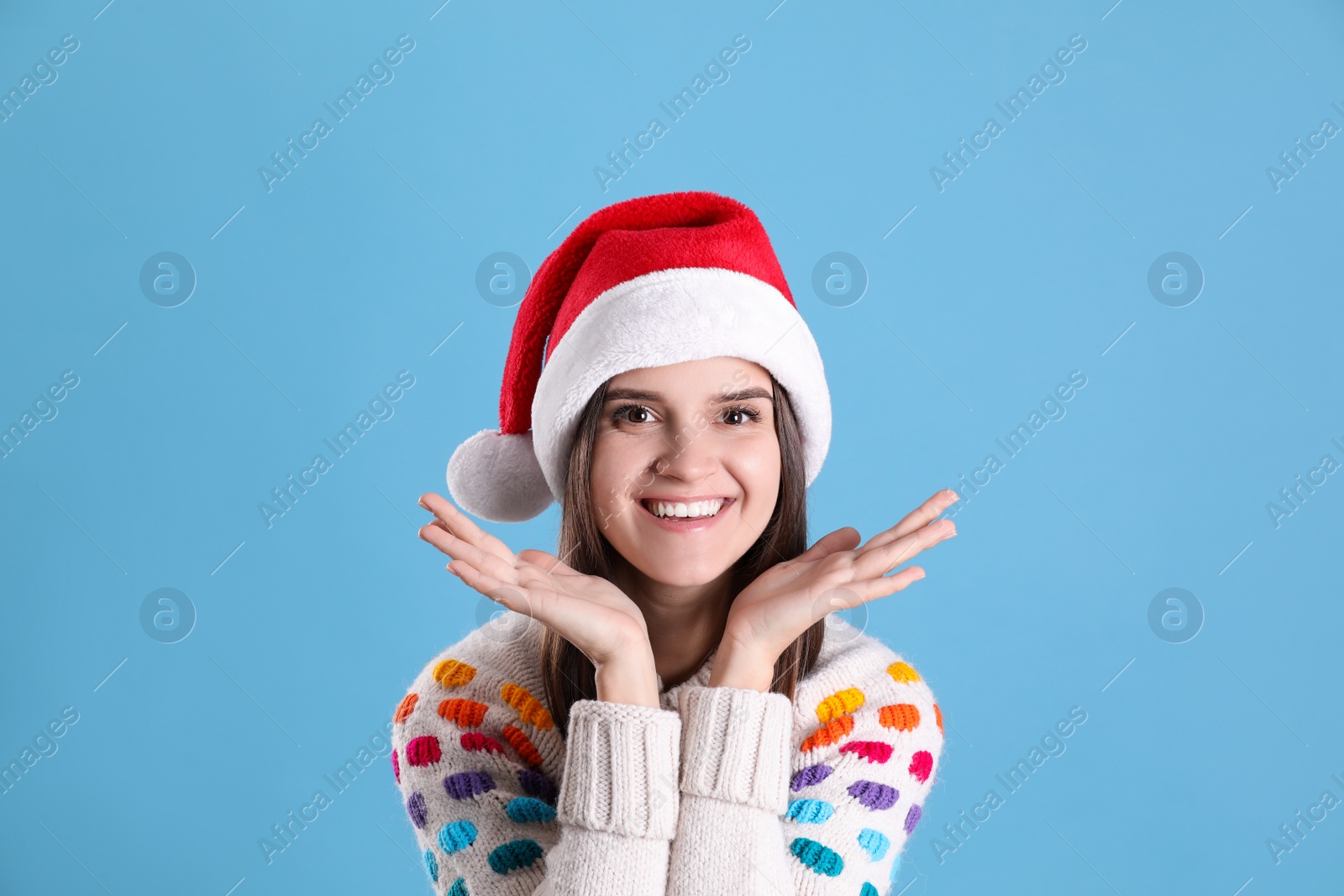 Photo of Pretty woman in Santa hat and festive sweater on light blue background