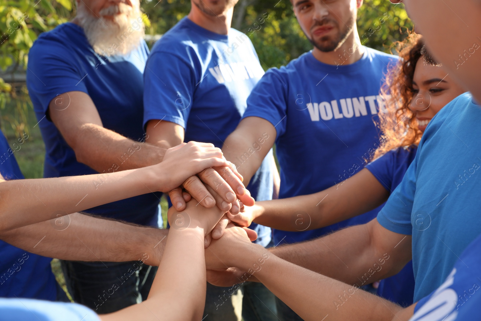 Photo of Group of volunteers joining hands together outdoors, closeup