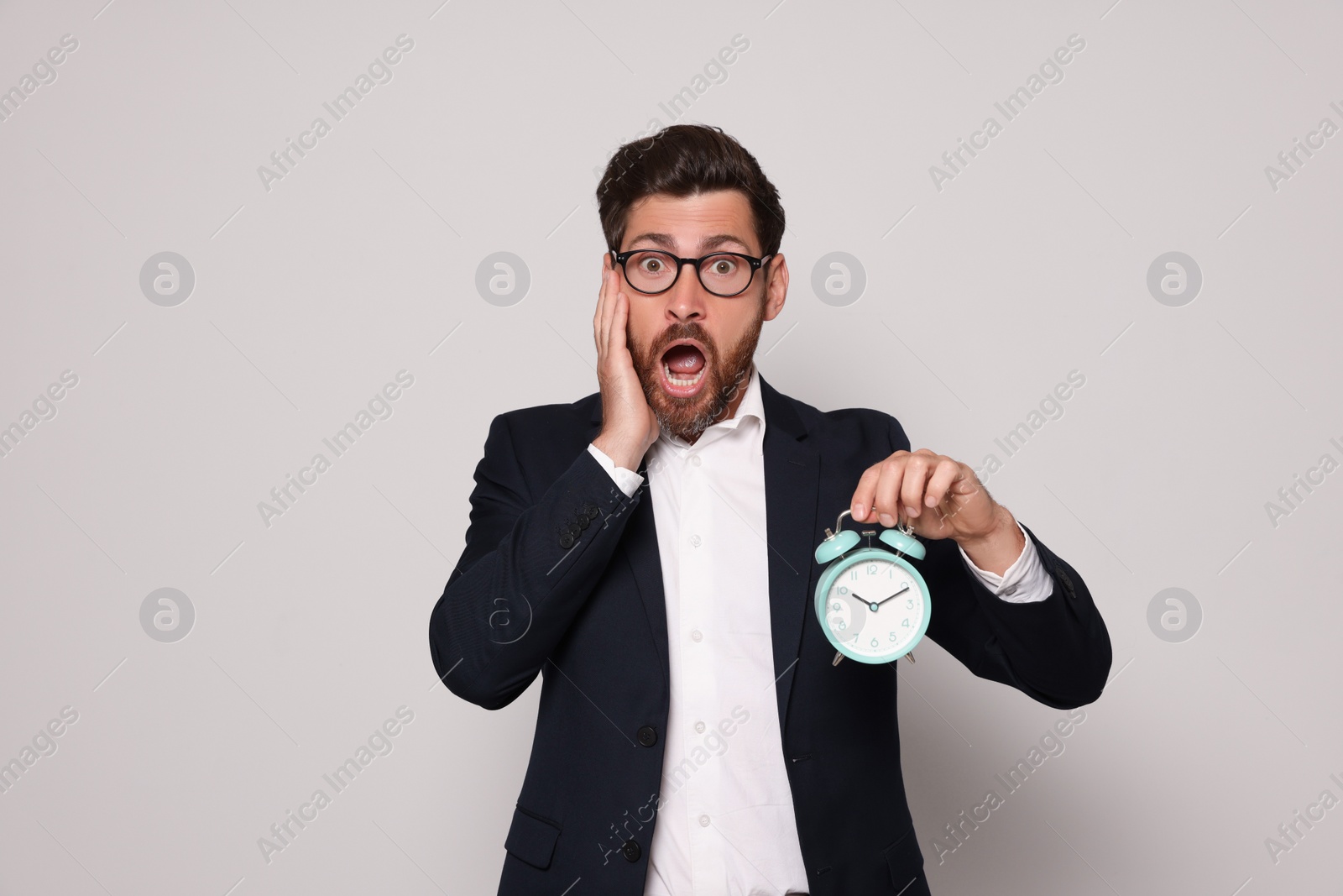 Photo of Emotional bearded man with alarm clock on light grey background. Being late concept