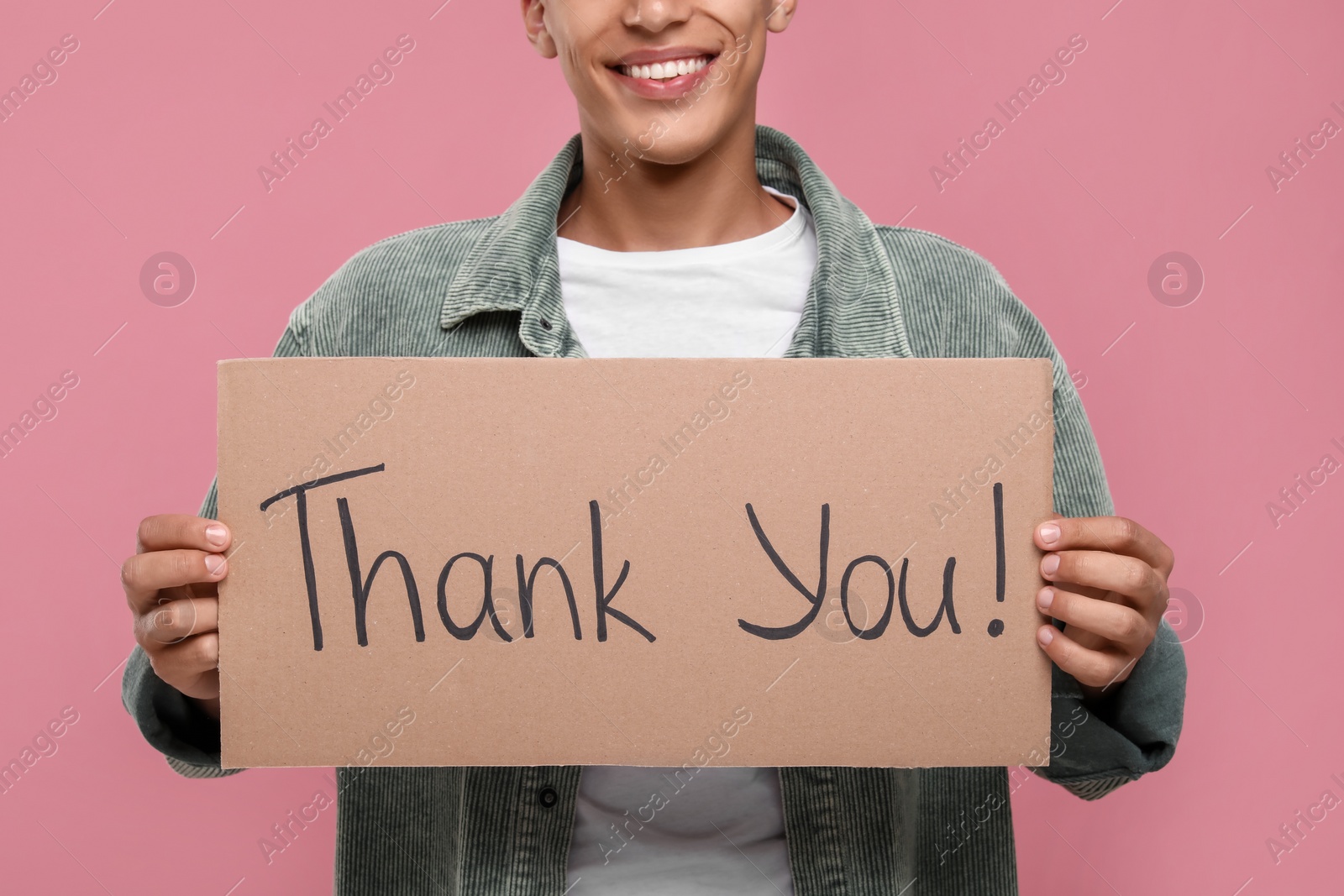 Photo of Man holding cardboard sheet with phrase Thank You on pink background, closeup