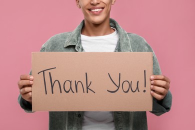 Photo of Man holding cardboard sheet with phrase Thank You on pink background, closeup