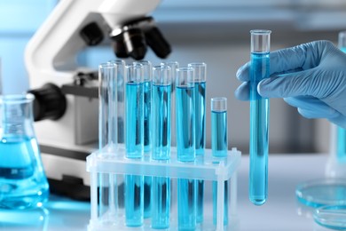 Scientist holding test tube with light blue liquid in laboratory, closeup