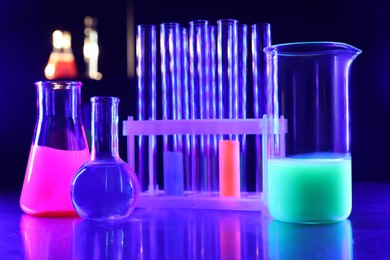 Laboratory glassware with luminous liquids on table against dark blue background