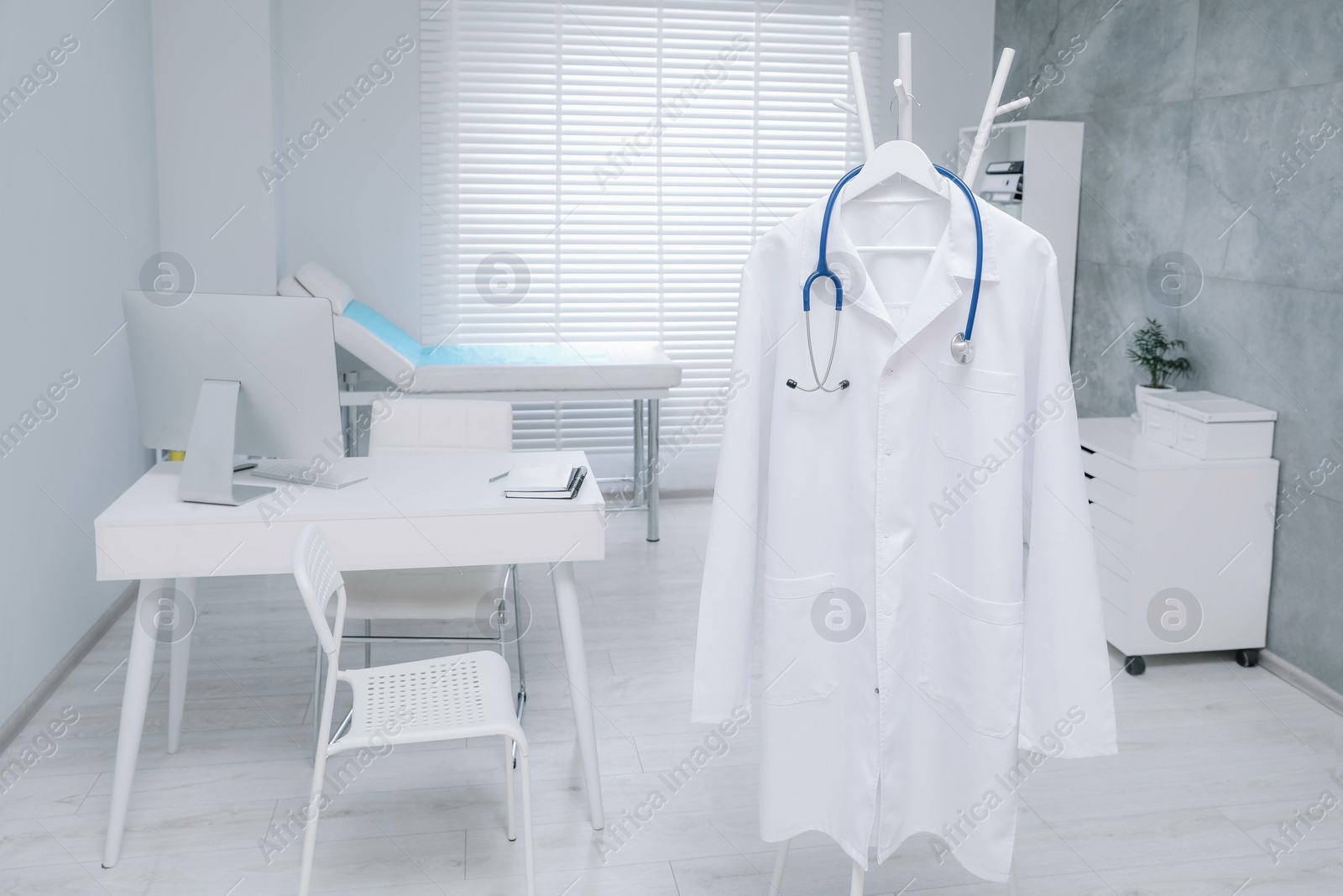 Photo of White doctor's gown and stethoscope hanging on rack in clinic