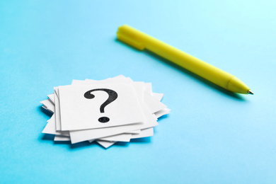 Photo of Heap of paper notes with question marks and pen on light blue background, closeup
