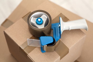 Photo of Adhesive tape dispenser on cardboard box indoors, closeup