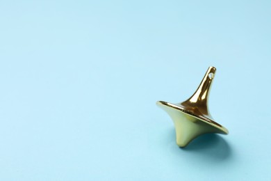 Photo of One golden spinning top on light blue background, closeup. Space for text