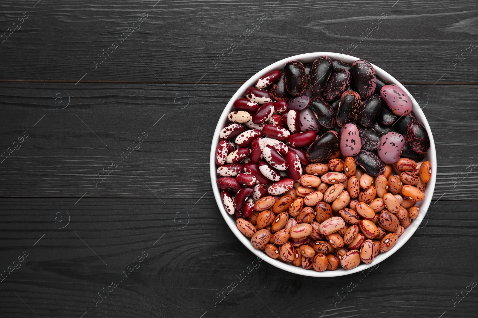 Photo of Different kinds of dry kidney beans in bowl on wooden table, top view. Space for text