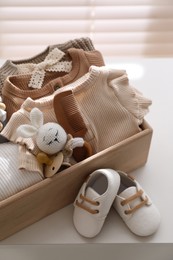 Wooden crate with children's clothes, toy and pacifier near shoes on white table in room