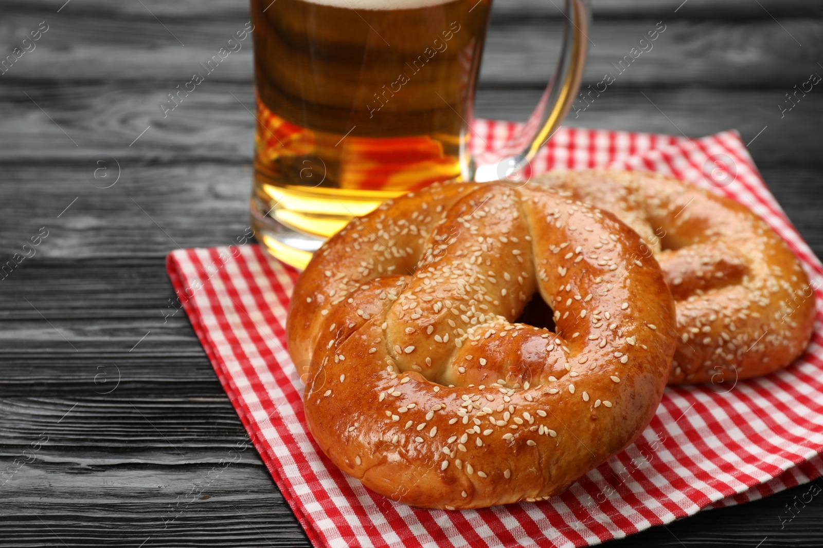 Photo of Tasty pretzels and glass of beer on black wooden table, closeup