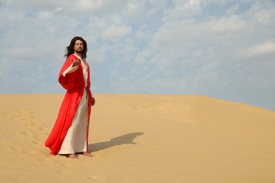 Photo of Jesus Christ with outstretched hand in desert. Space for text