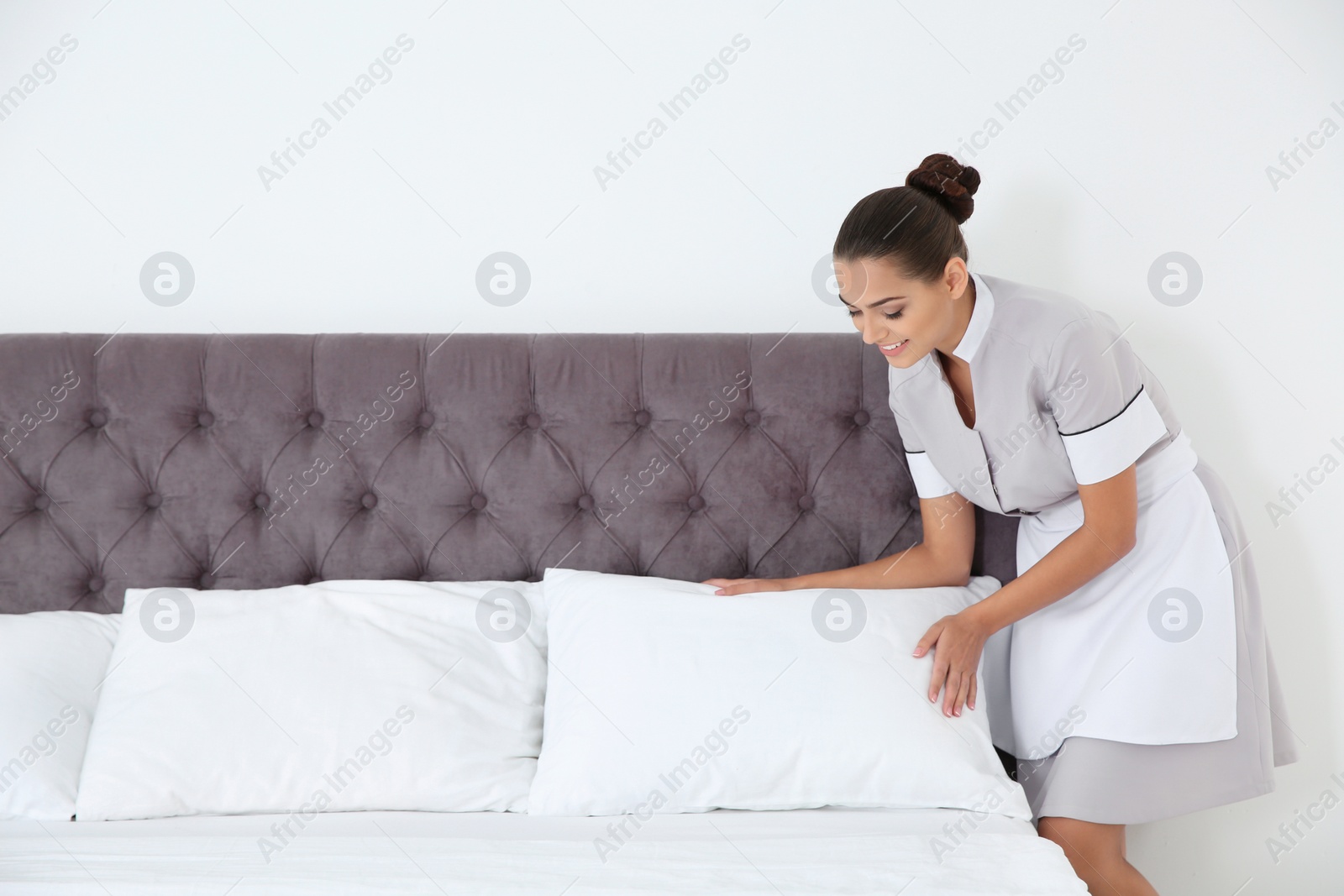 Photo of Young chambermaid making bed in hotel room