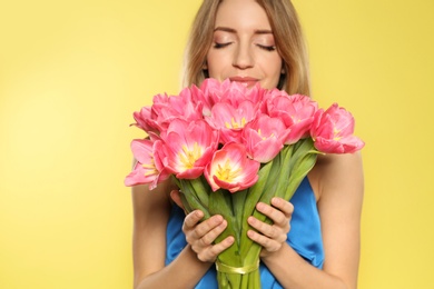 Photo of Portrait of beautiful smiling girl with spring tulips on yellow background. International Women's Day