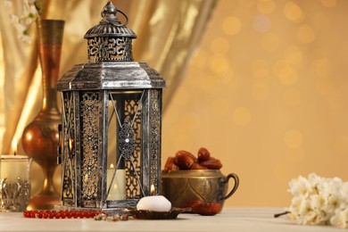 Photo of Arabic lantern, misbaha, candles, dates and flowers on table against blurred lights