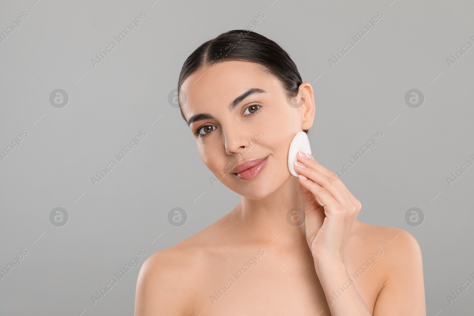 Photo of Beautiful woman removing makeup with cotton pad on light grey background, space for text