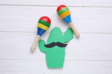 Colorful maracas and paper cactus with mustache on white wooden table, flat lay. Musical instrument