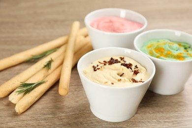 Photo of Different kinds of tasty hummus served with bread sticks on wooden table