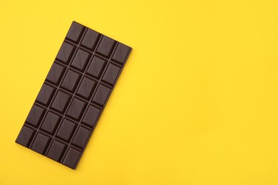 Photo of Tasty chocolate bar on yellow background, top view. Space for text