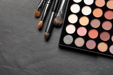 Photo of Beautiful eye shadow palette and brushes on dark grey textured table, flat lay. Space for text