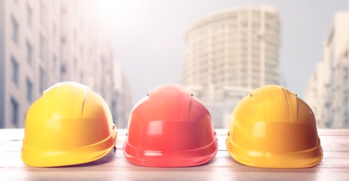 Image of Hard hats on wooden surface at construction site with unfinished building. Banner design