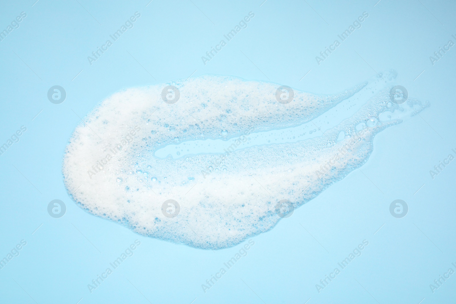 Photo of Smudge of white washing foam on light blue background, top view