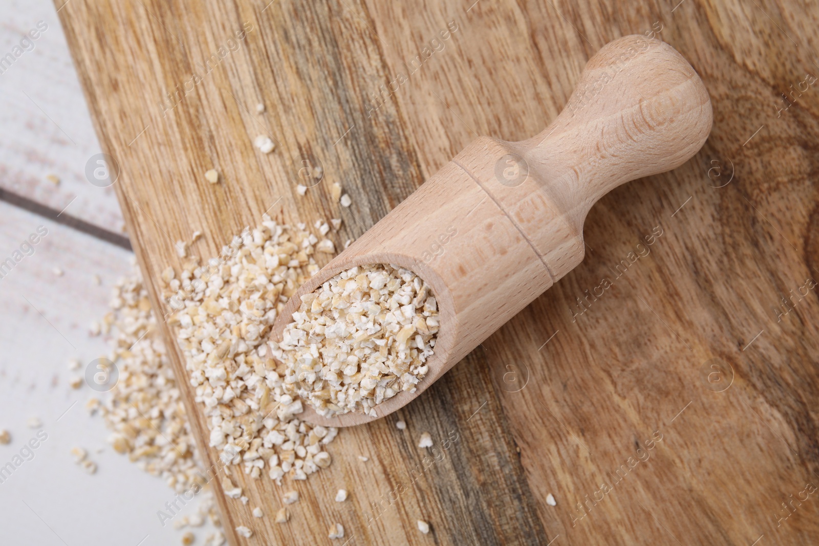 Photo of Scoop with raw barley groats on light wooden table, top view