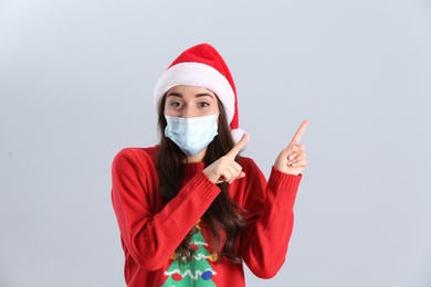 Beautiful woman wearing Santa Claus hat and medical mask on light grey background