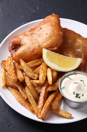 Photo of Tasty fish, chips, lemon and sauce on black table, closeup